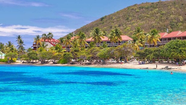 A beachfront hotel with multiple red-roofed buildings, palm trees, and a clear blue sea. - Walk To The Beach From This Beautifull New Studio With Everything You Need (St. Thomas)