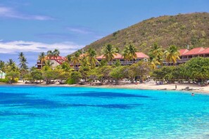Un hotel frente a la playa con varias edificaciones de techos rojos, palmeras y un mar azul cristalino.