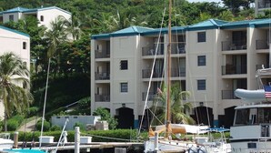 A marina with boats docked, a building with balconies, and lush greenery in the background. - Walk To The Beach From This Beautifull New Studio With Everything You Need (St. Thomas)