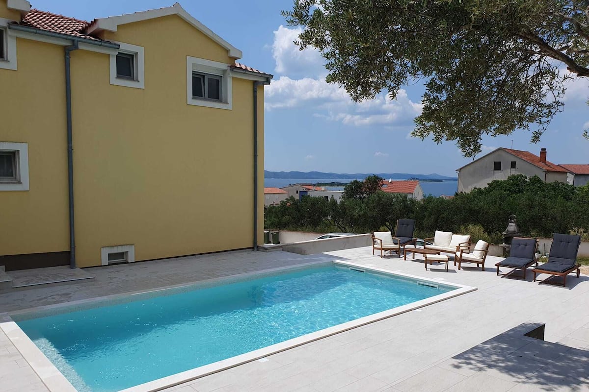 A swimming pool with lounge chairs and a view of the sea.