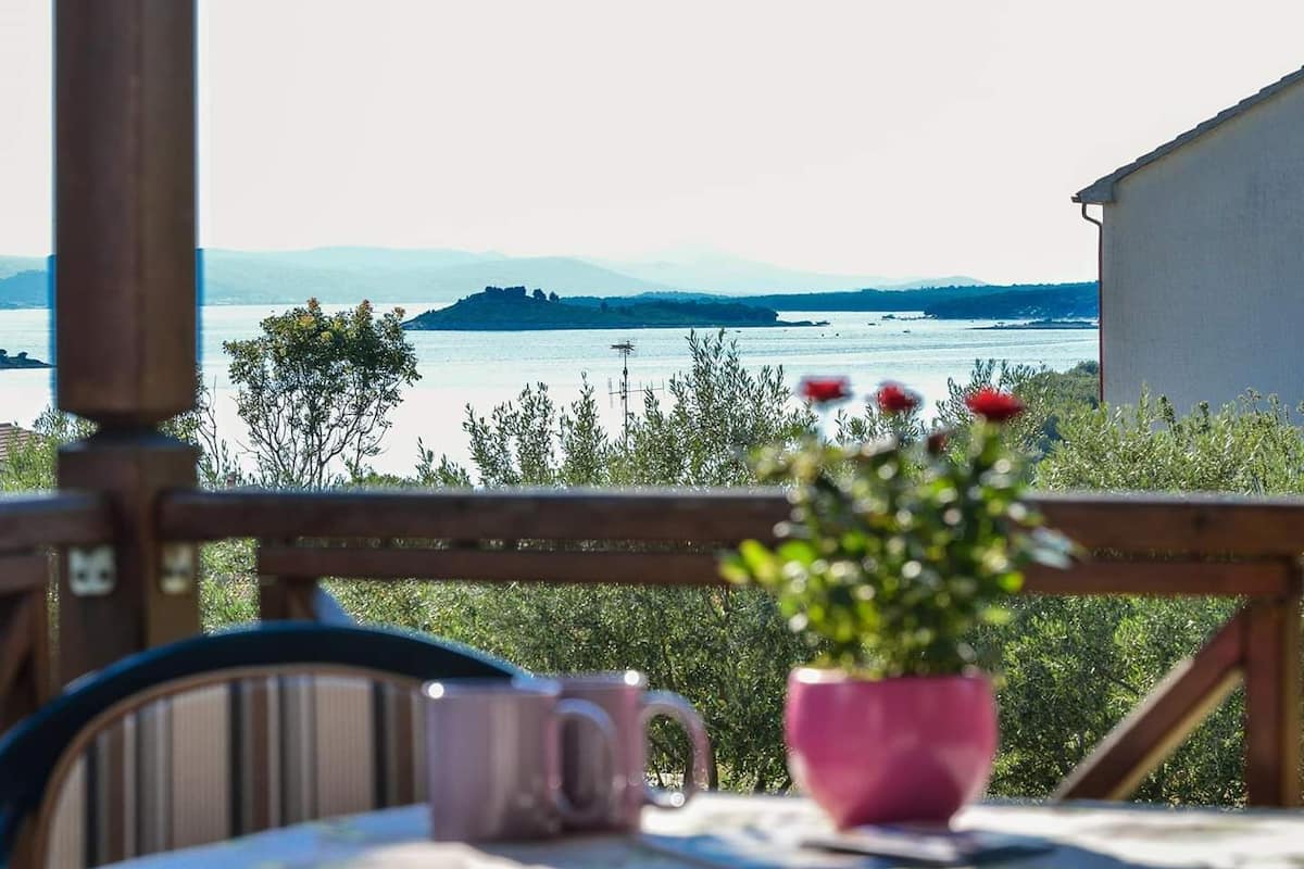A table with a pink mug and a potted plant, overlooking a lake with distant mountains.