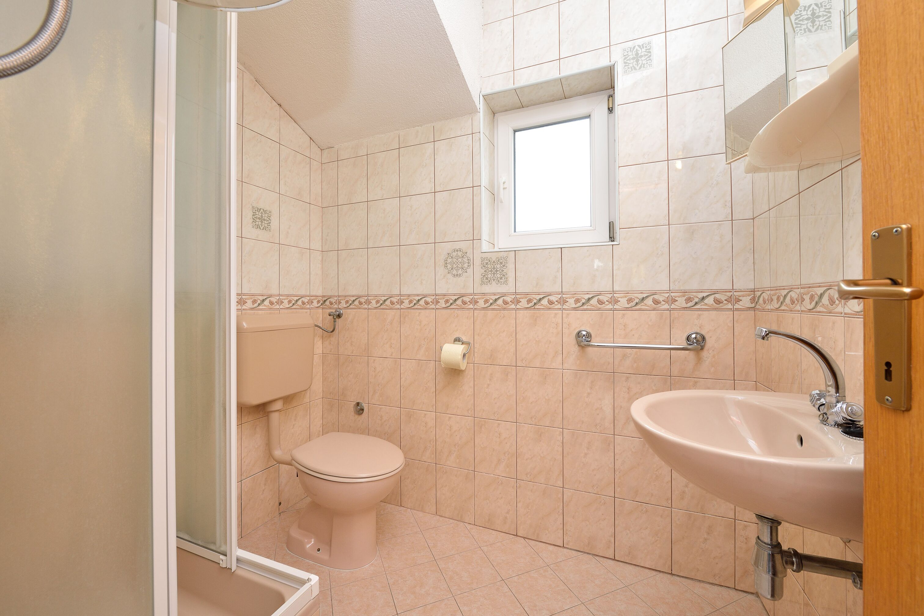 A bathroom with a toilet, sink, and a small window.