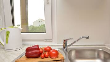 A kitchen with a stainless steel sink, a wooden cutting board with tomatoes and a red bell pepper, and a white kettle with a green handle.