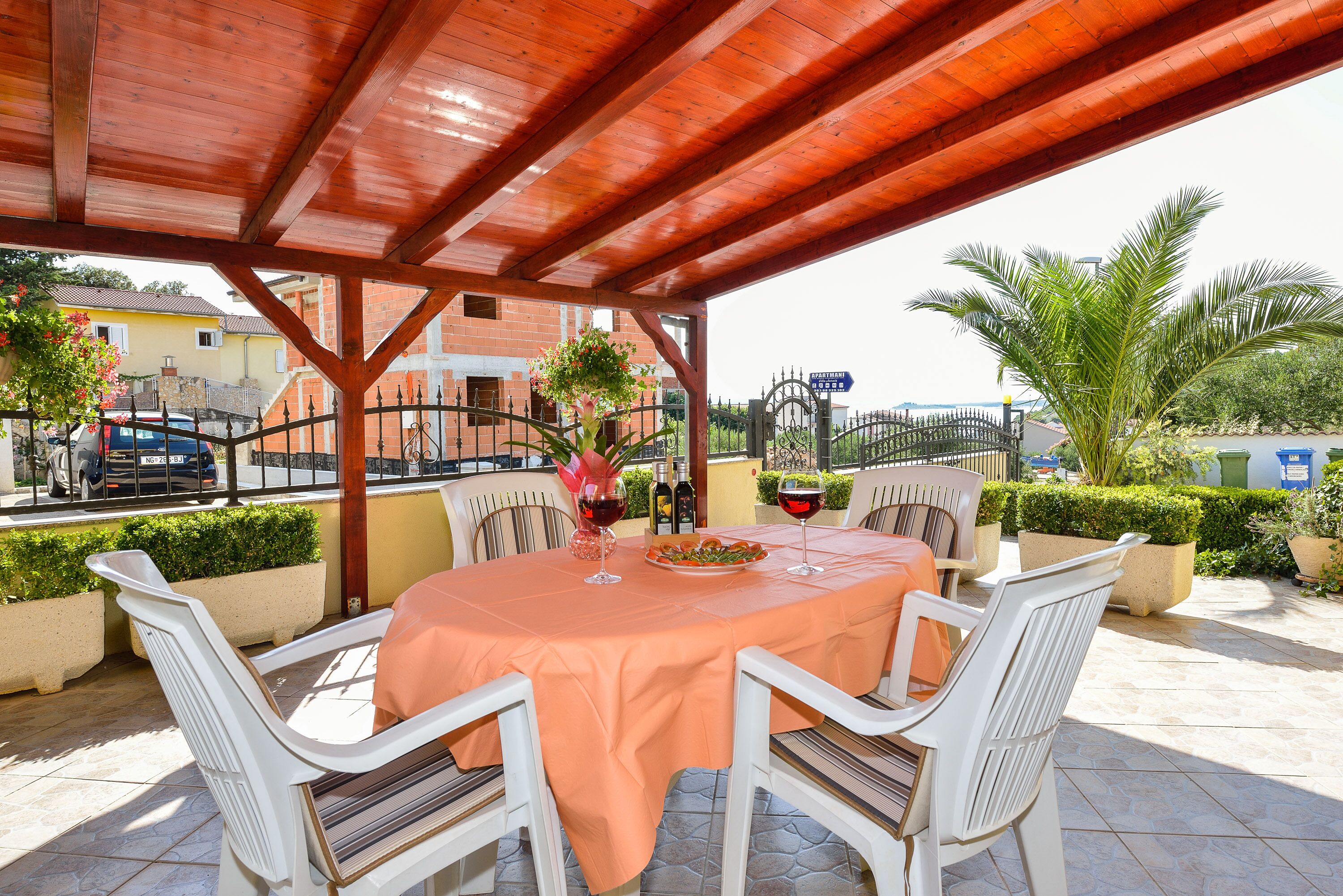 An outdoor patio with a table set for two, surrounded by white chairs, under a wooden pergola.