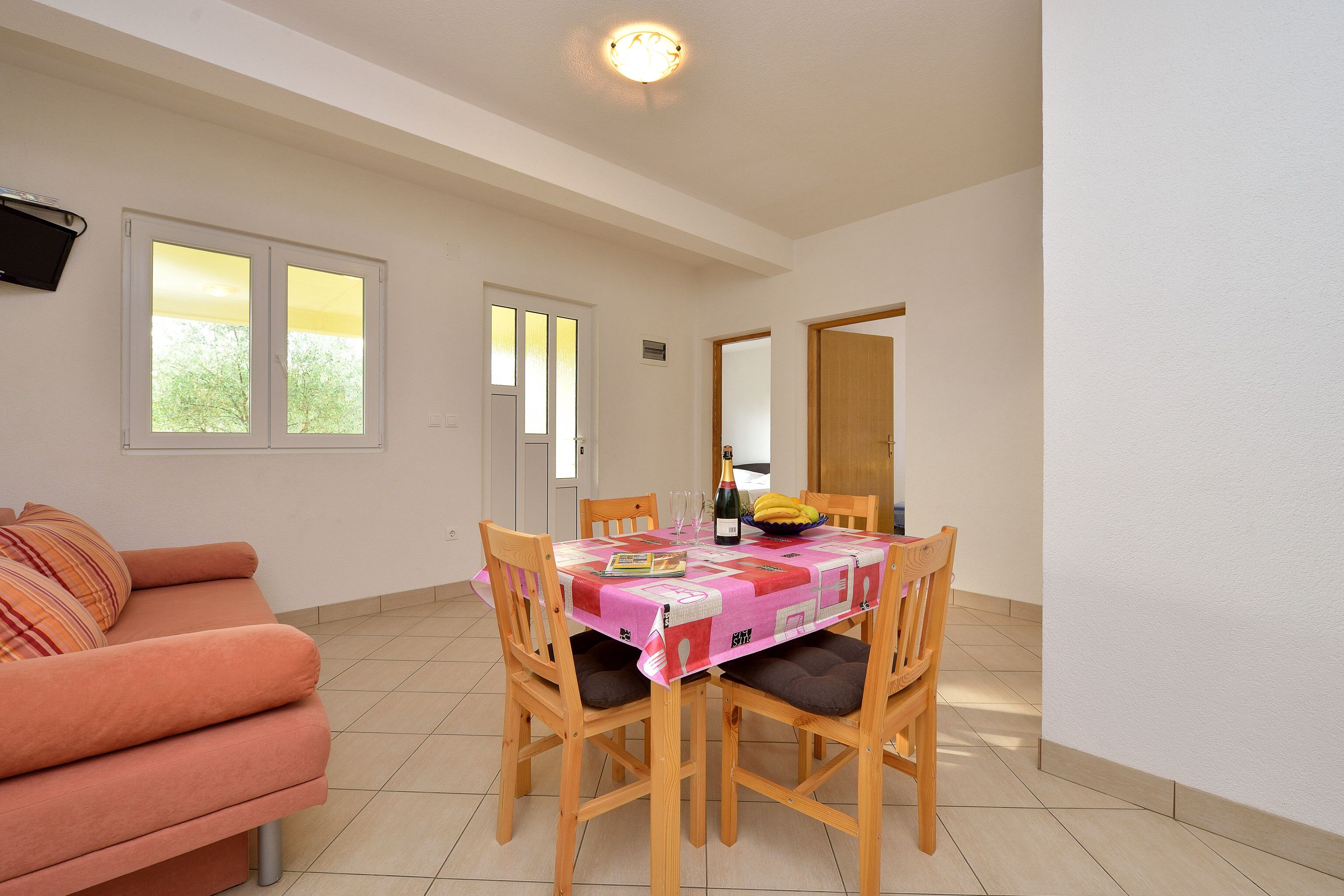 A dining area with a table set for four, a sofa, and a window with a view of greenery.