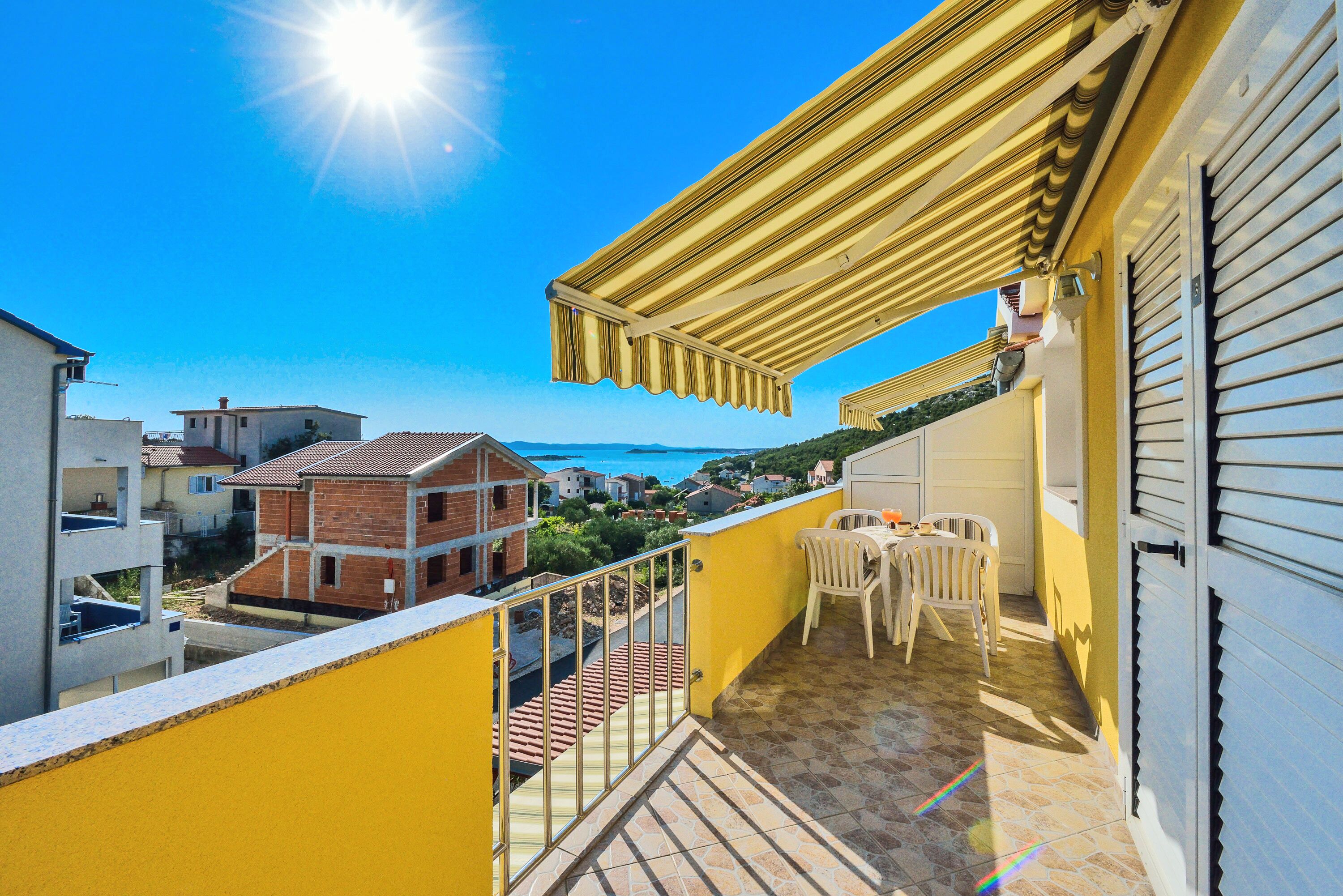 Un balcone con vista sul mare, ringhiera gialla e pavimento piastrellato.