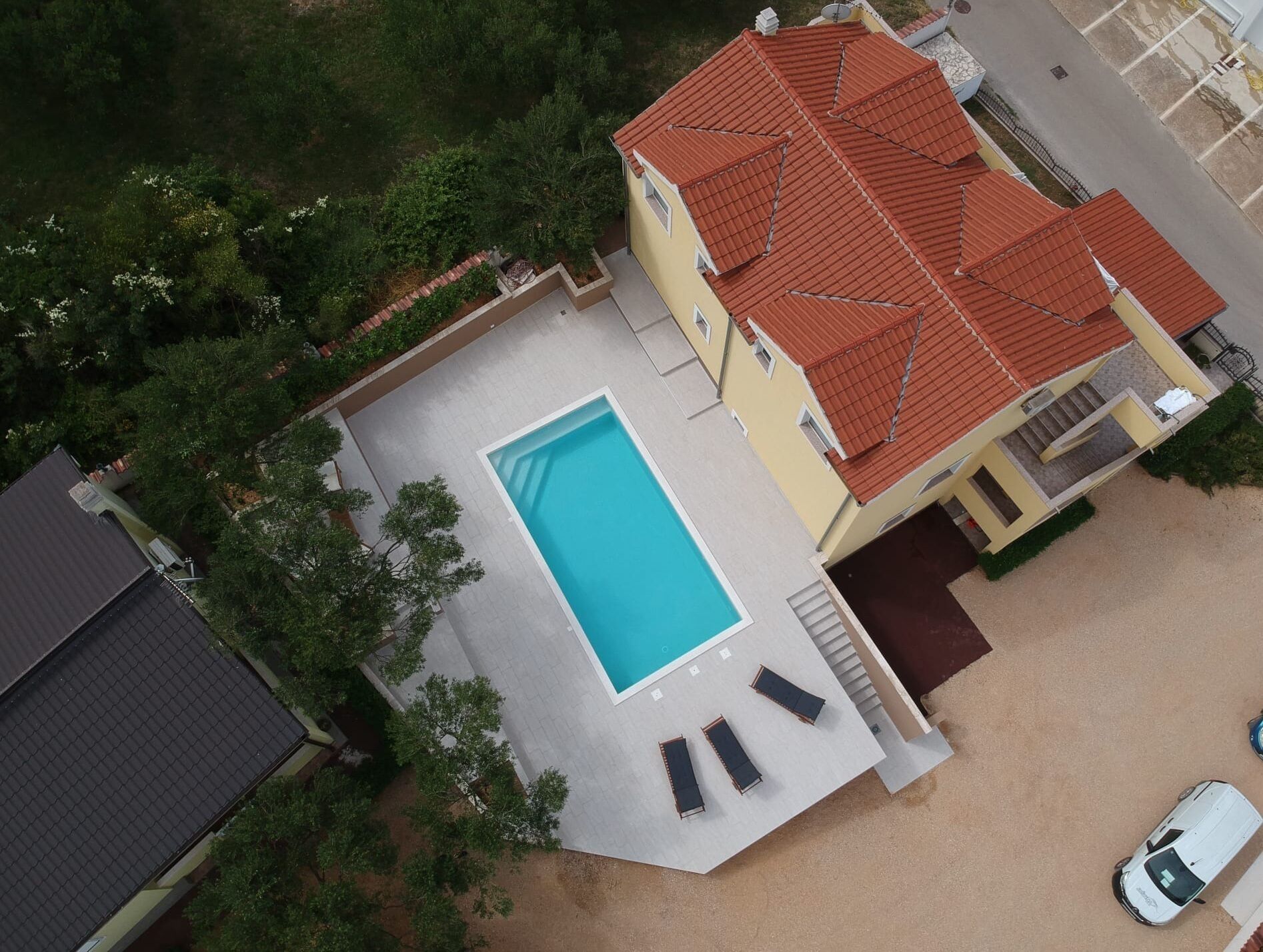 Vue aérienne d’une propriété résidentielle dotée d’une piscine, d’un patio couvert et d’une voiture garée à proximité.