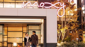 Un edificio moderno con un letrero de neón que dice “moxy” sobre la entrada.