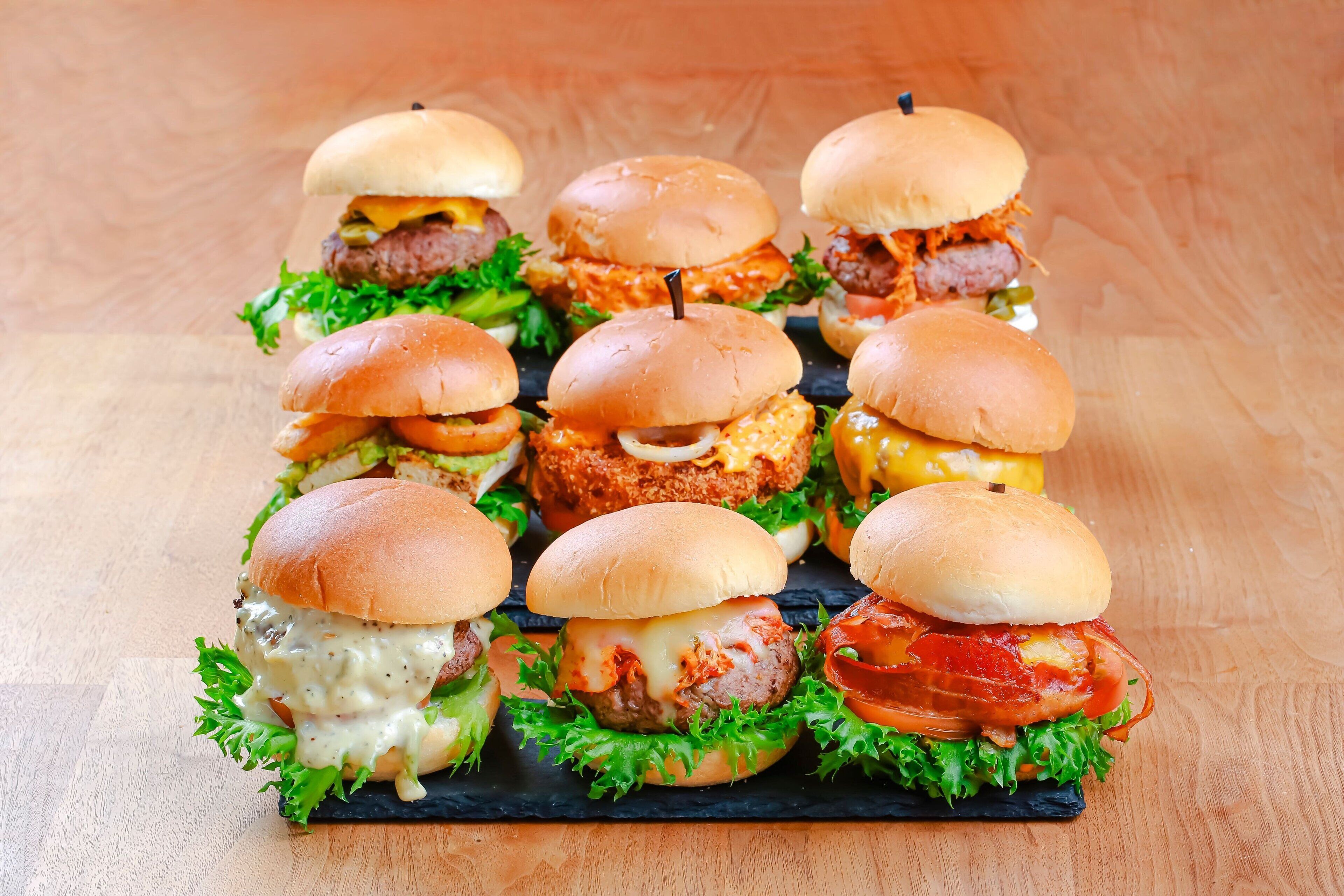 A tray of assorted burgers with various toppings and sauces, arranged on a black slate board.