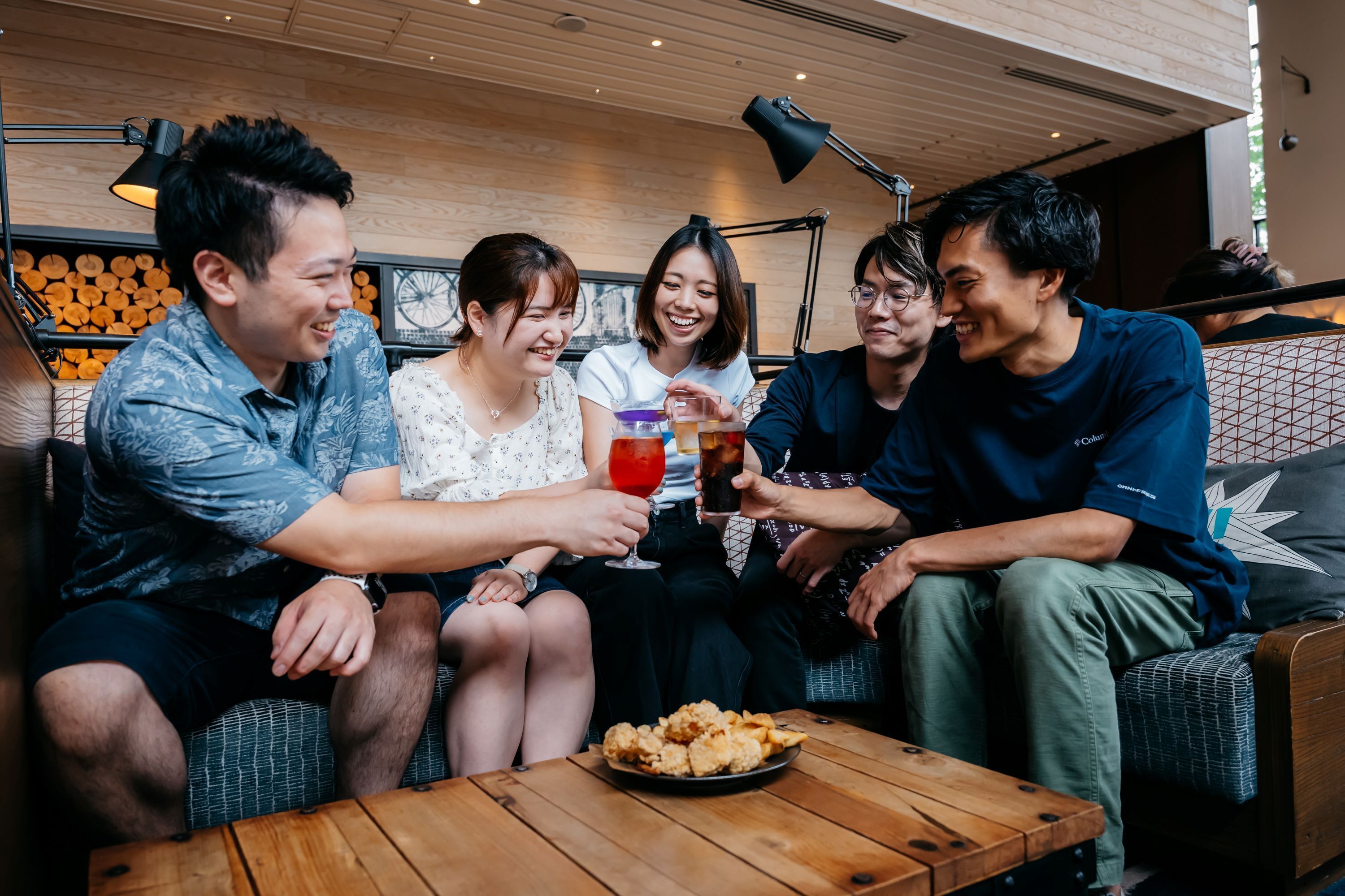 A group of people sitting on a couch, holding drinks and eating snacks.