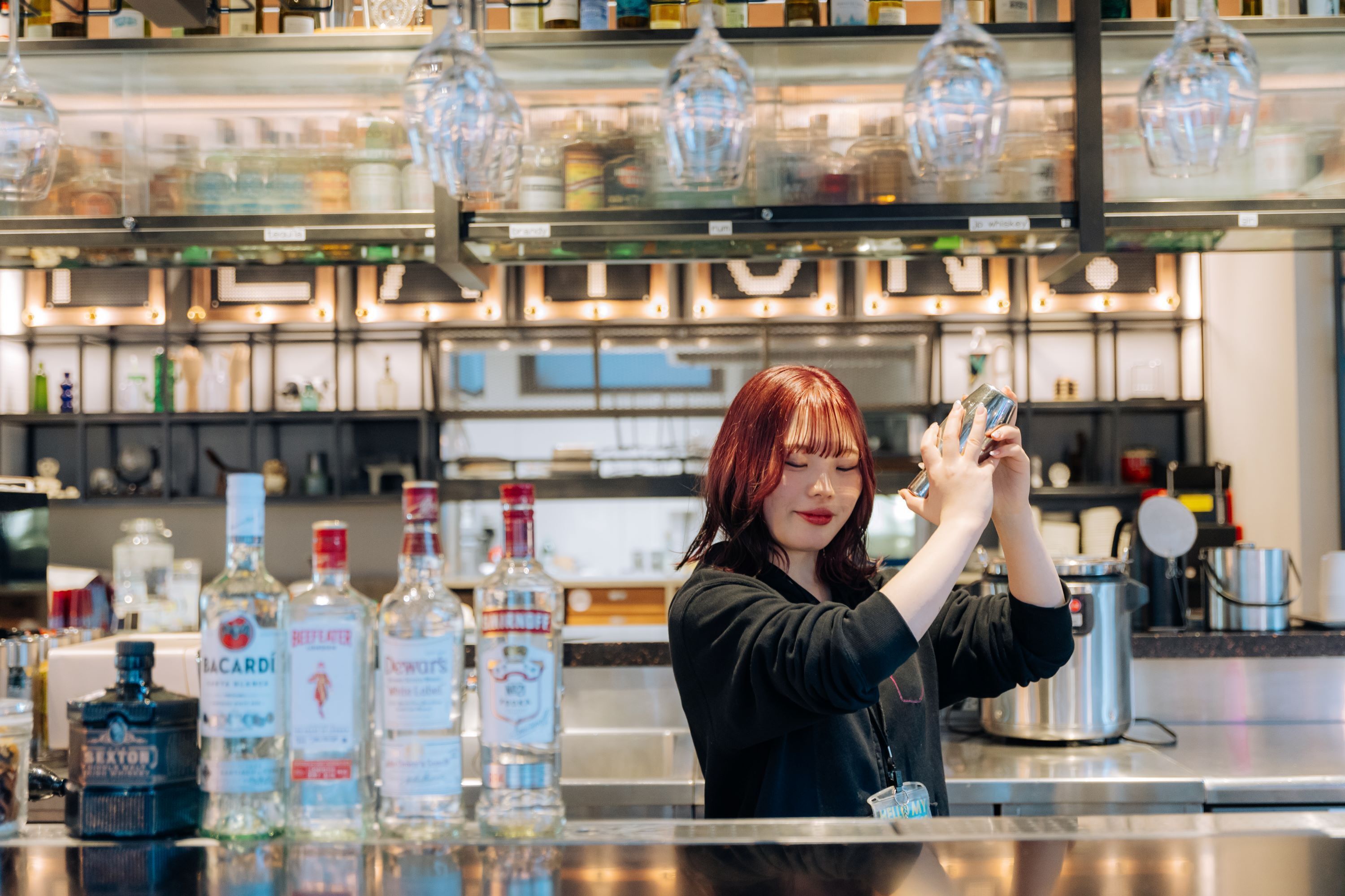 A bar area with various bottles of liquor, a person holding a glass, and overhead lighting.