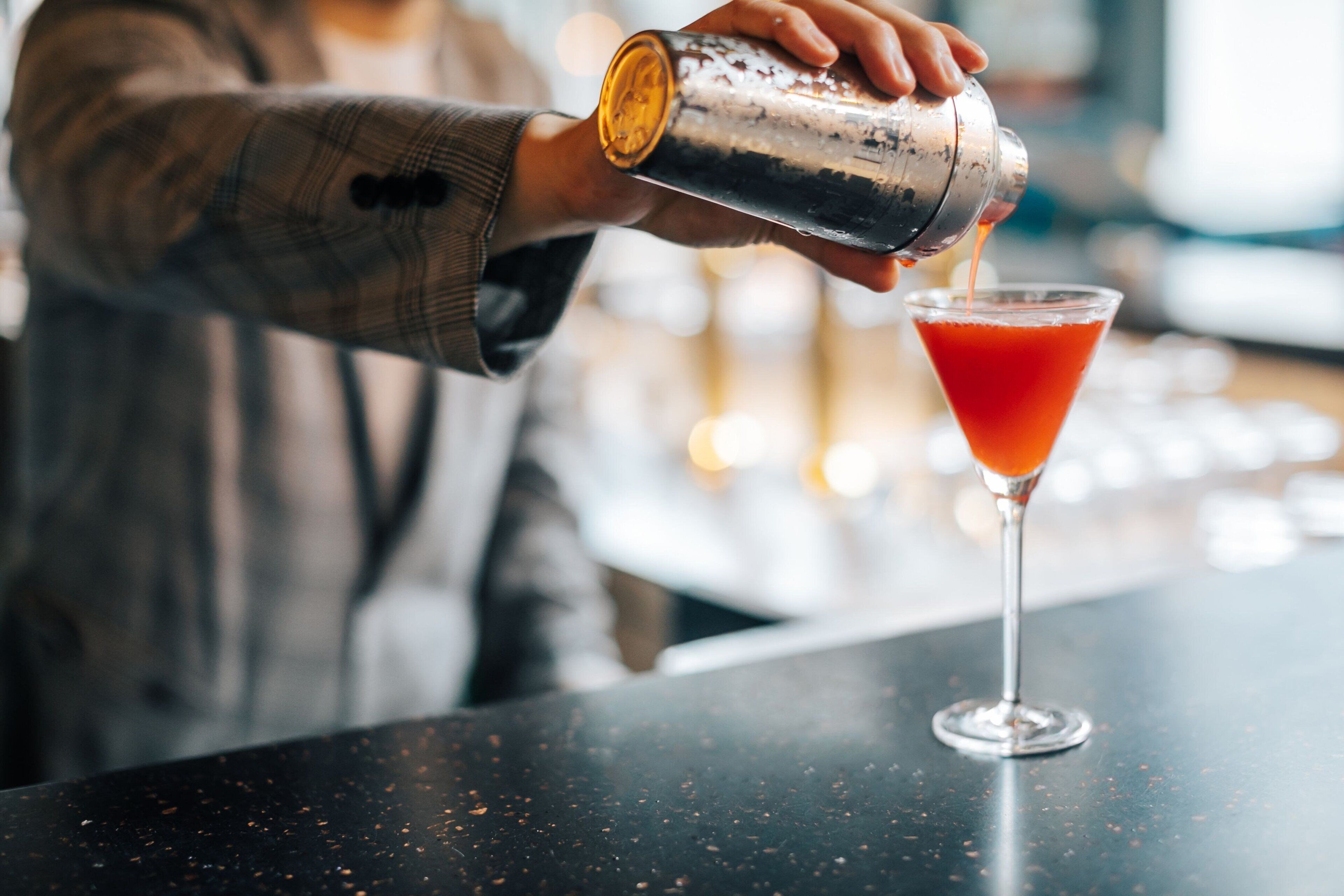 A person pouring a drink into a martini glass.