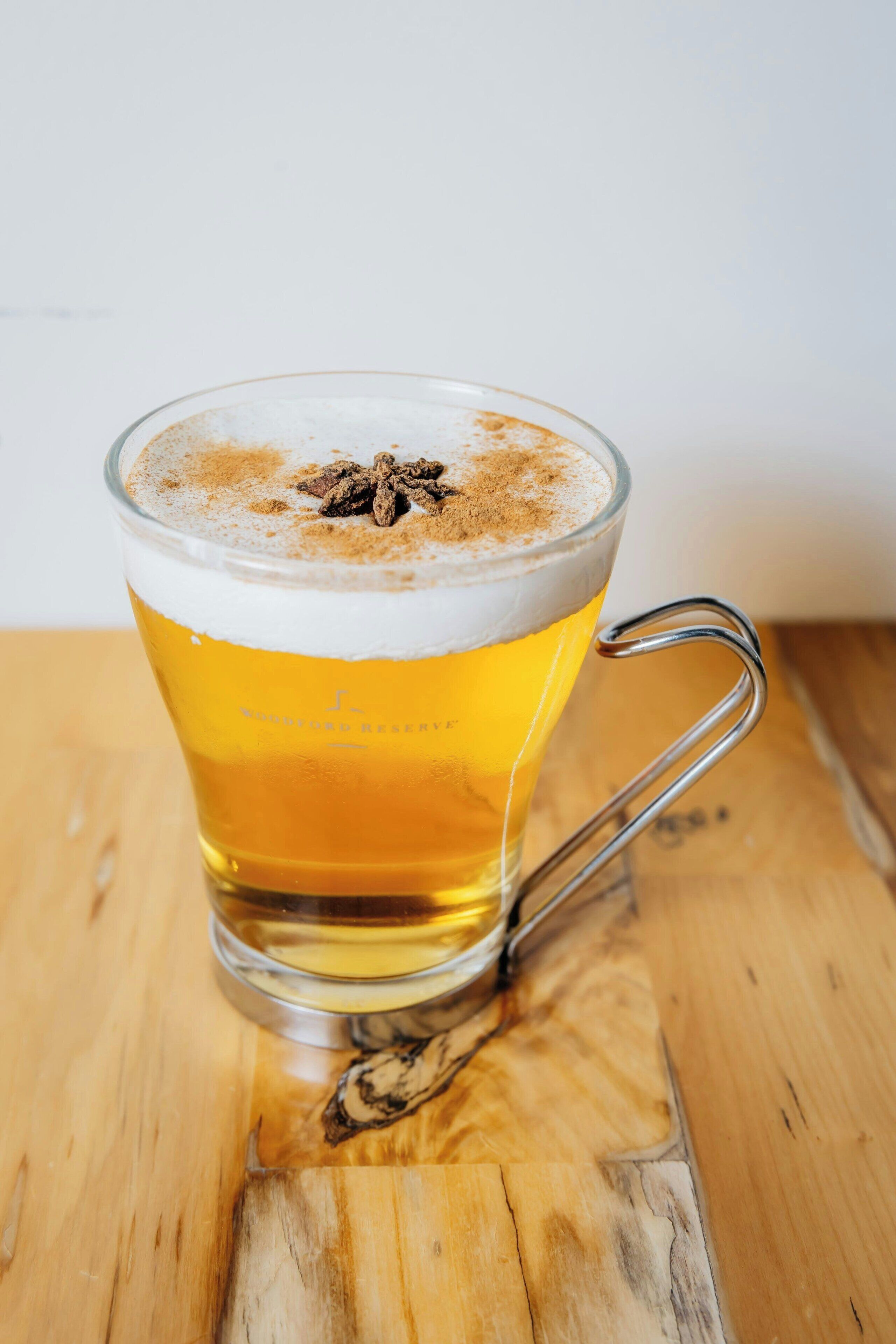 Un vaso de cerveza con espuma y especias sobre una mesa de madera.
