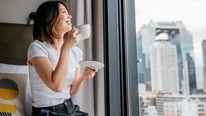 Una persona sentada junto a una ventana con vista a la ciudad, sosteniendo una taza.