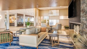 Un hall d’hôtel moderne avec un canapé, des fauteuils, un coin repas et un téléviseur fixé au mur.