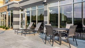 Une terrasse extérieure avec une table et des chaises, une porte-fenêtre et un mur en briques.