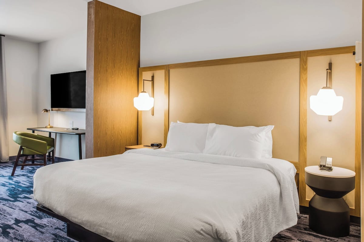 Une chambre d’hôtel avec un grand lit, un bureau et deux lampes fixées au mur.