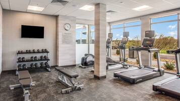 Un gimnasio con cintas de correr, bancos de pesas y mancuernas.
