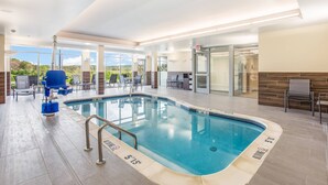 Une piscine intérieure à l’eau claire, dotée d’un poste de surveillance pour le sauveteur et d’un mur en verre offrant une vue sur l’extérieur.