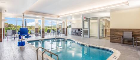An indoor swimming pool with clear water, a lifeguard chair, and a glass wall offering a view of the outdoors.