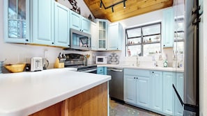 A modern kitchen with light blue cabinets, stainless steel appliances, and a wooden ceiling.