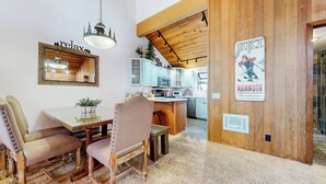 A dining area with a wooden table and chairs, a hanging light fixture, and a kitchen in the background. - Updated & Large, Near Golf Course! Gas Grill & Deck. Forested Quiet Location (Mammoth Lakes)