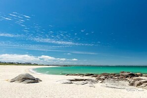 A beach with clear turquoise water, white sand, and scattered rocks.