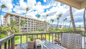 A balcony with a view of a hotel building, palm trees, and a clear sky. - Kihei Akahi #C-520  Tastefully Updated, Corner Studio on 5th Floor, A/C (Kihei)