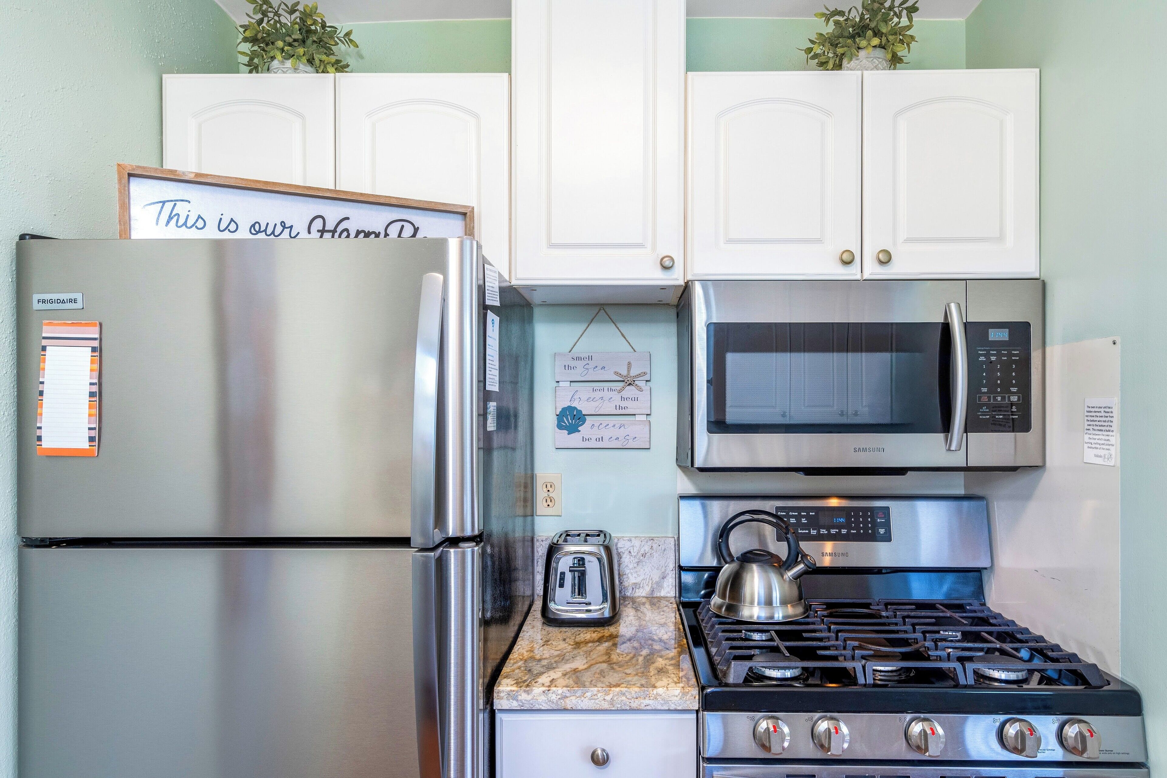 A compact kitchen with a stainless steel refrigerator, a microwave, a toaster, and a gas stove.