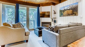 Un salon chaleureux avec une cheminée, un canapé, une table basse et une grande fenêtre avec des rideaux.