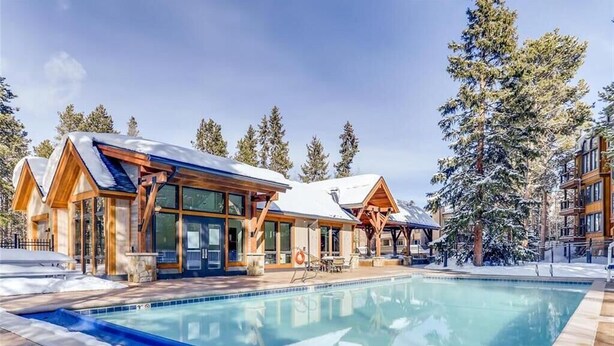 Un chalet moderne doté d’une piscine, d’une façade en bois et entouré d’arbres couverts de neige.