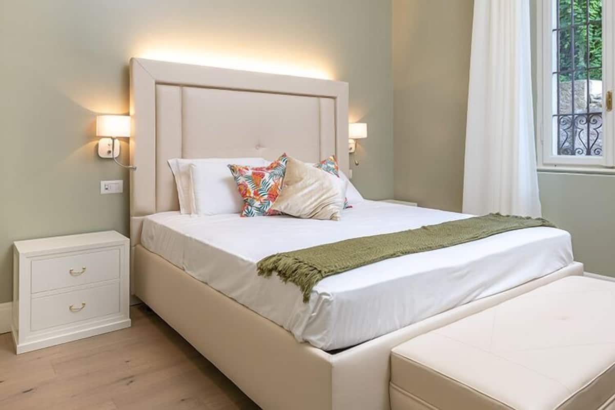Een keurig opgemaakt slaapkamer met een bed, nachtkastjes en een raam met uitzicht.