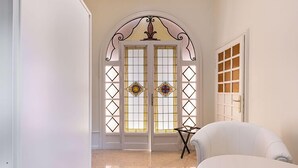 Um corredor com uma cadeira branca, uma porta com vitrais e um chão de azulejos.