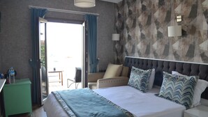 Habitación de hotel con una cama grande, una mesita de noche verde, una silla y vistas al exterior a través de una puerta corrediza.