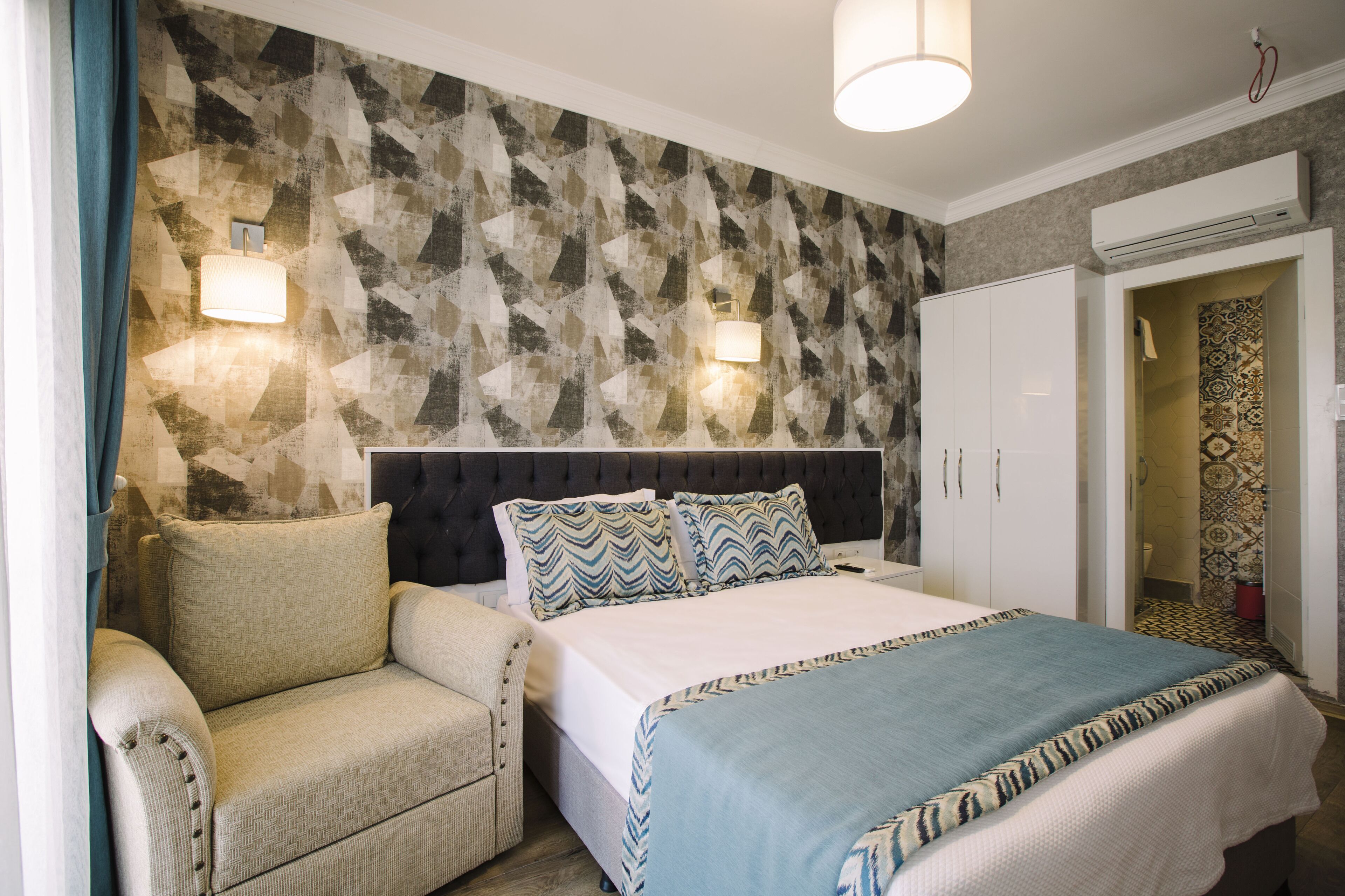 A hotel room with a bed, a sofa, a wall-mounted light fixture, and a wardrobe.