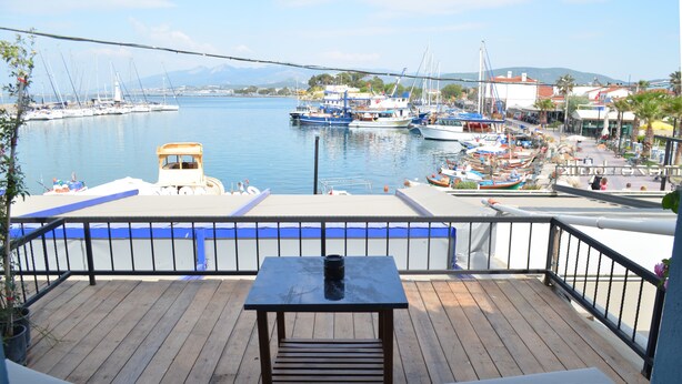 Una terraza de madera con una mesa y sillas, con vista a un puerto deportivo lleno de barcos y un paisaje urbano distante.