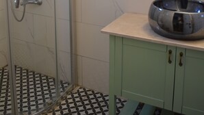 Un baño con cabina de ducha de vidrio, un lavabo y un mueble de tocador con armarios verdes.