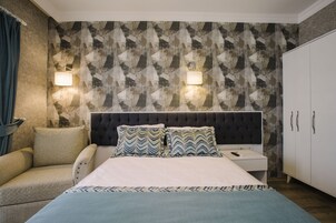 Un dormitorio con pared estampada, cabecero capitonado, mesita de noche con lámpara y armario.