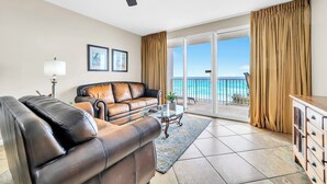 Sala de estar com sofá de couro, mesa de centro de vidro e vista para o mar através de uma porta de correr.