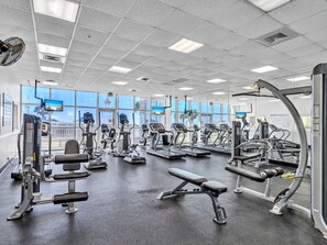 Een sportschool met diverse fitnessapparaten, grote ramen en uitzicht op buiten.