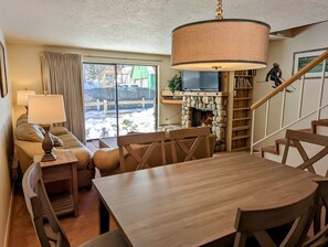 Una sala de estar acogedora con chimenea, televisor, mesa de comedor y una escalera.
