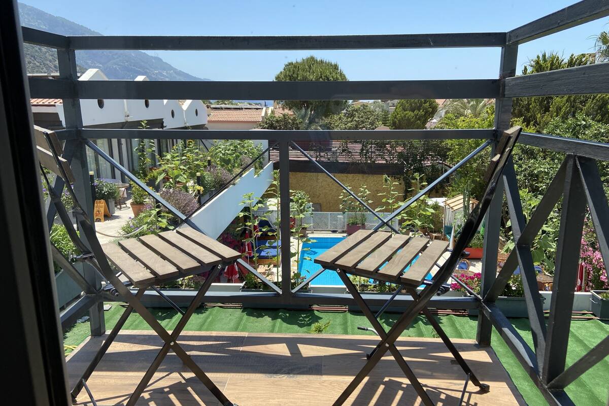 A balcony with a view of a pool and greenery, featuring two wooden chairs.