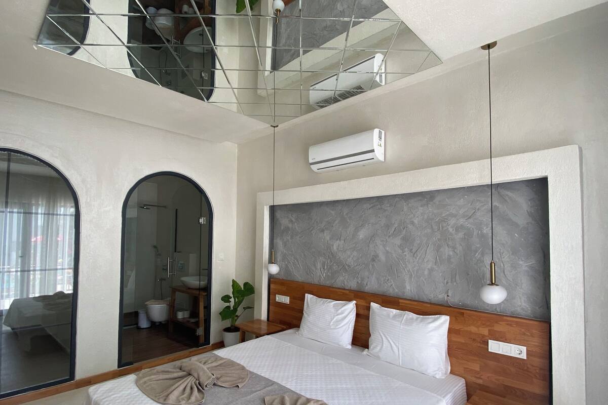 A modern hotel room with a large bed, a wooden headboard, and a large mirror.