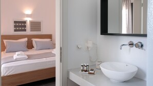A modern hotel room with a neatly made bed, a large mirror above the sink, and a small table with toiletries. - Vorta Naxos - Adults Only (Naxos)