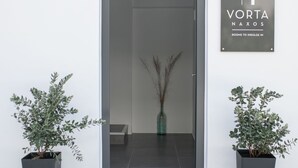 A modern entrance with a glass door, two potted plants, and a sign reading "VORTA NAXOS ROOMS TO INDULGE IN". - Vorta Naxos - Adults Only (Naxos)
