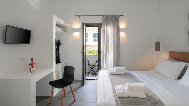 A hotel room with a bed, a desk with a chair, a TV, and a view of the outside balcony. - Vorta Naxos - Adults Only (Naxos)