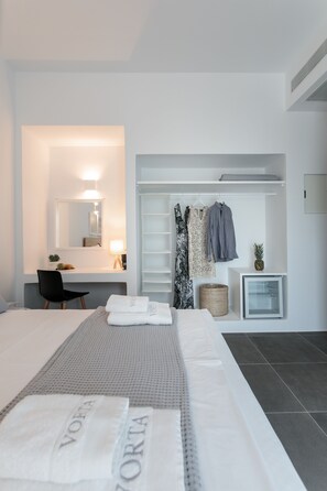 A modern hotel room with a neatly made bed, a desk with a chair, a wardrobe, and a small refrigerator. - Vorta Naxos - Adults Only (Naxos)