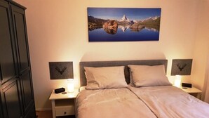 A bedroom with a bed, two bedside tables, a nightstand, a wardrobe, and a wall-mounted picture. - Breitkopf vacation apartment with south-facing terrace and mountain view (Reit im Winkl)