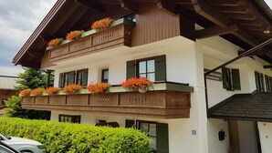 A two-story building with wooden balconies, green shutters, and flower boxes. - Breitkopf vacation apartment with south-facing terrace and mountain view (Reit im Winkl)