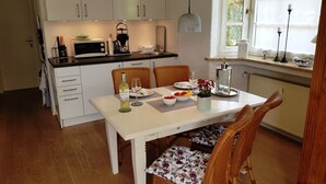 A compact kitchen with white cabinets, a dining table set for two, and a window with curtains. - Breitkopf vacation apartment with south-facing terrace and mountain view (Reit im Winkl)